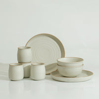 A white stoneware dinnerware set including cups, bowls, and plates with a swirl pattern on a white background.