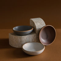 A set of ceramic sauce dishes in varying shades of white and brown, displayed against a dark background.